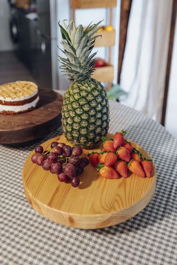 Una piña, uvas y fresas sobre una bandeja de madera redonda con soportes