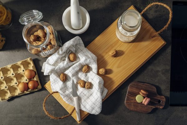 Nueces, un bote de harina, un trapo de cocina, un mortero de mármol y tres huevos sobre una bandeja fabricada en madera y cuerda como asas