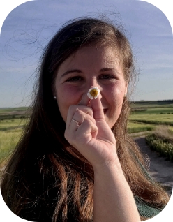 Chica posando en el campo sujetando una margarita a la altura de la nariz